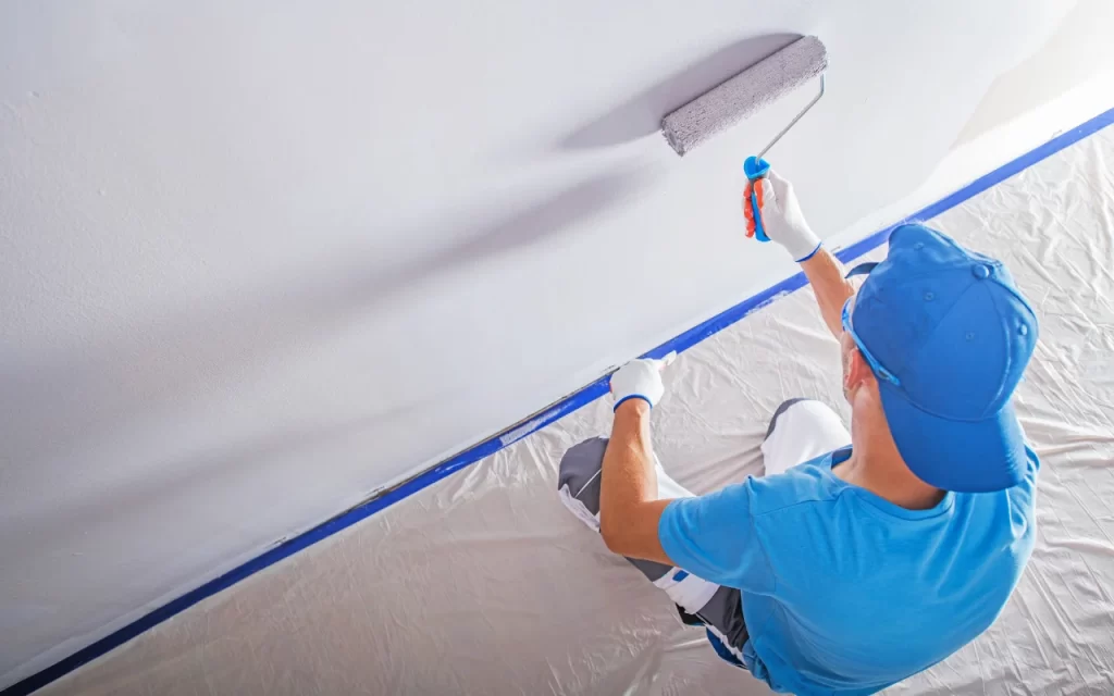 Painter taping edges and covering floors before painting a room
